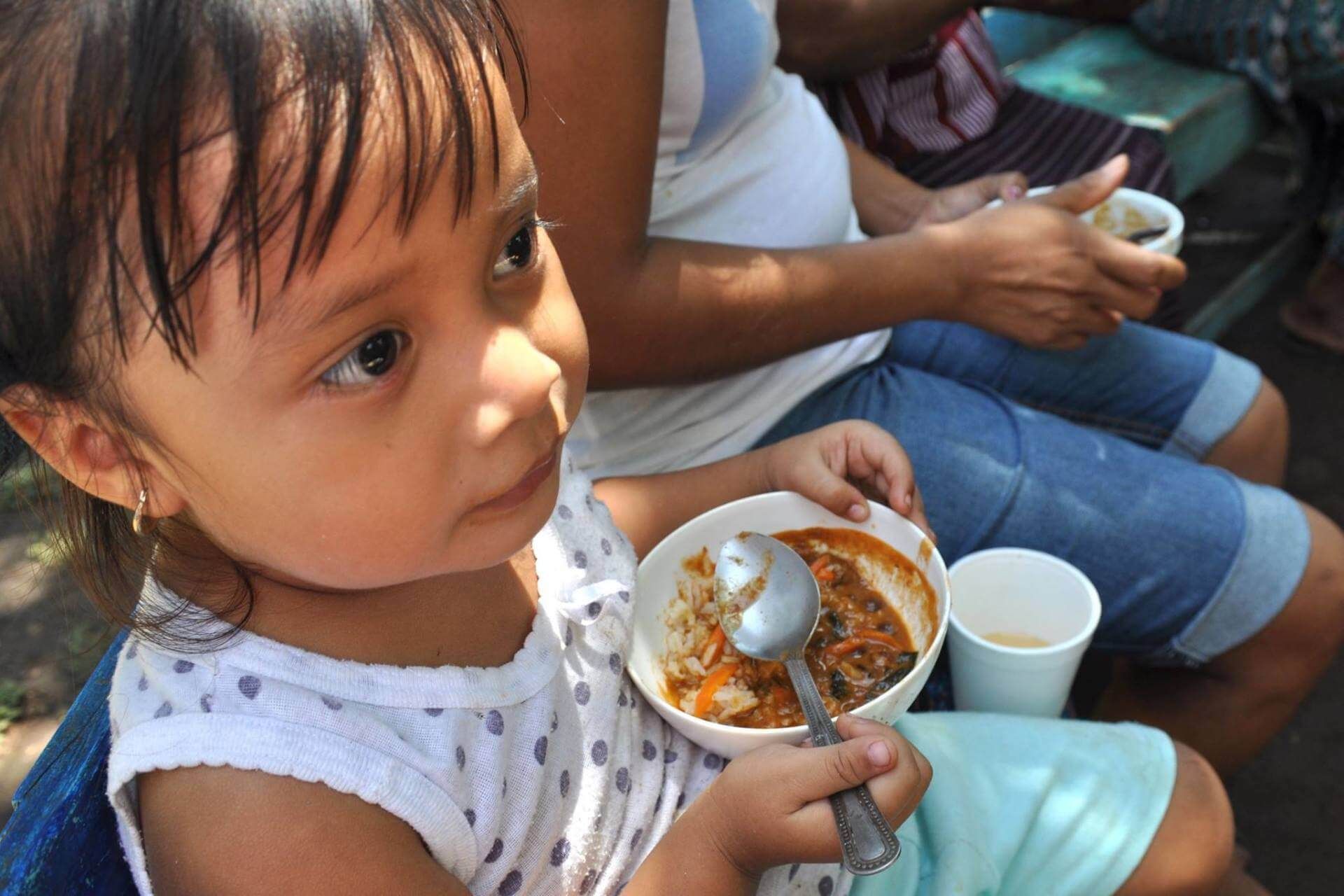 A little girl is eating from a bowl with a spoon