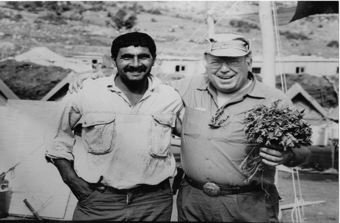 Two men are posing for a picture and one is holding a bouquet of flowers.