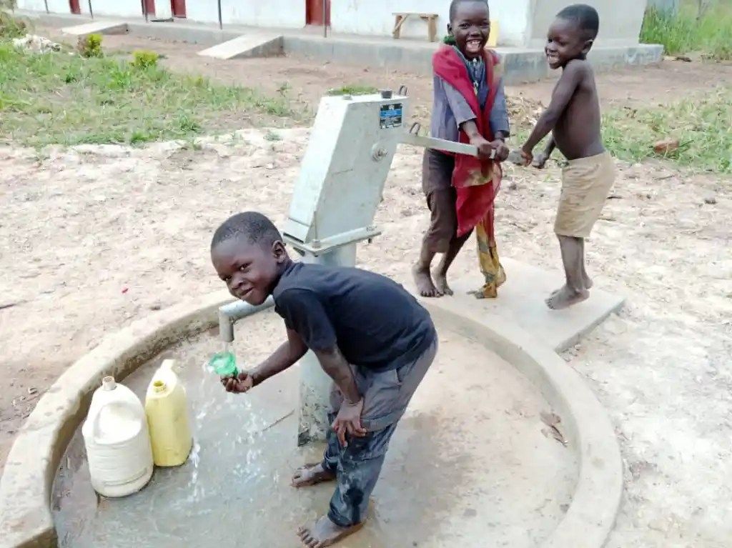A group of children are standing around a water fountain.