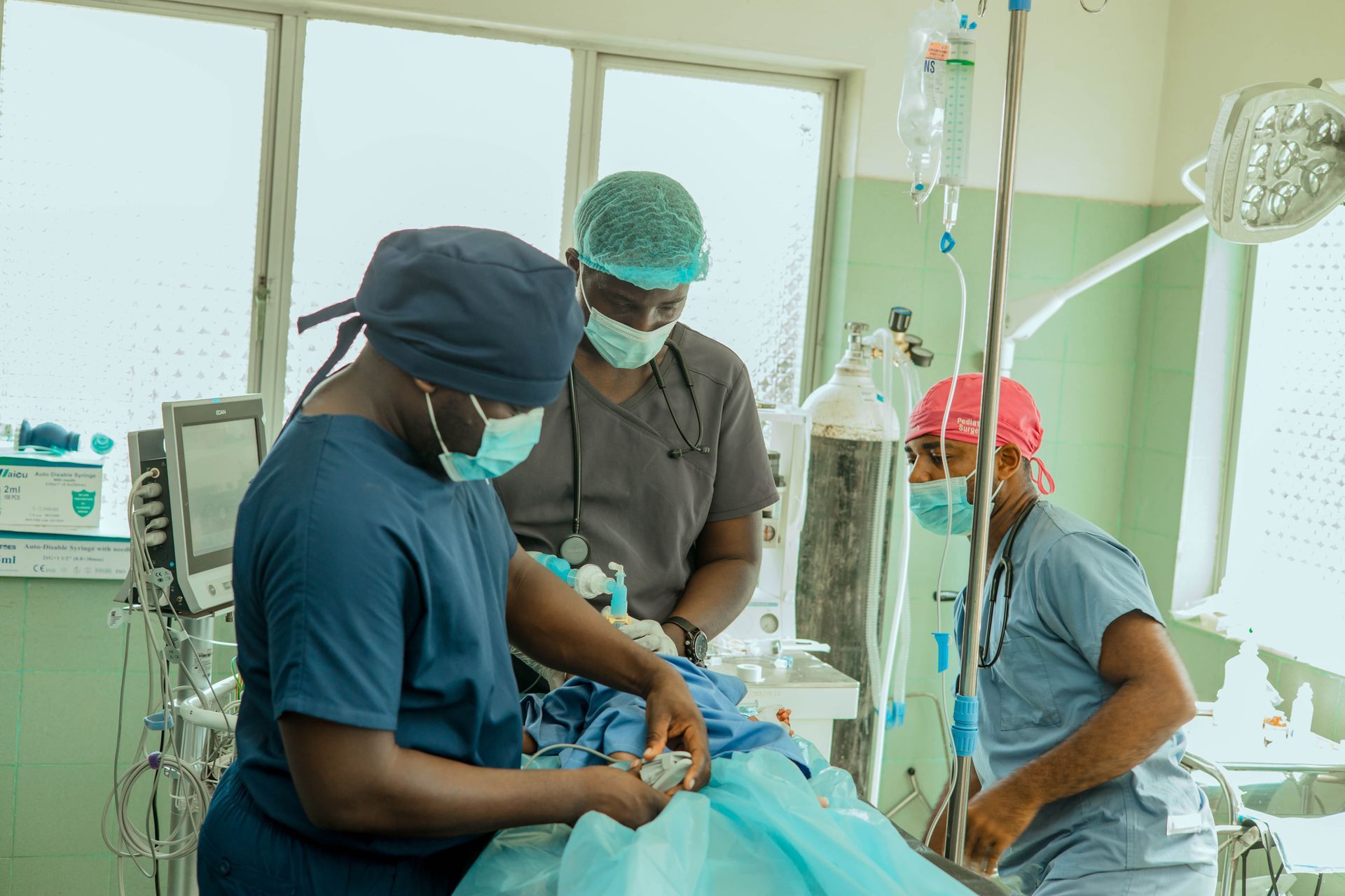 Medical professionals in blue and gray scrubs perform a surgical procedure in an operating room with equipment.