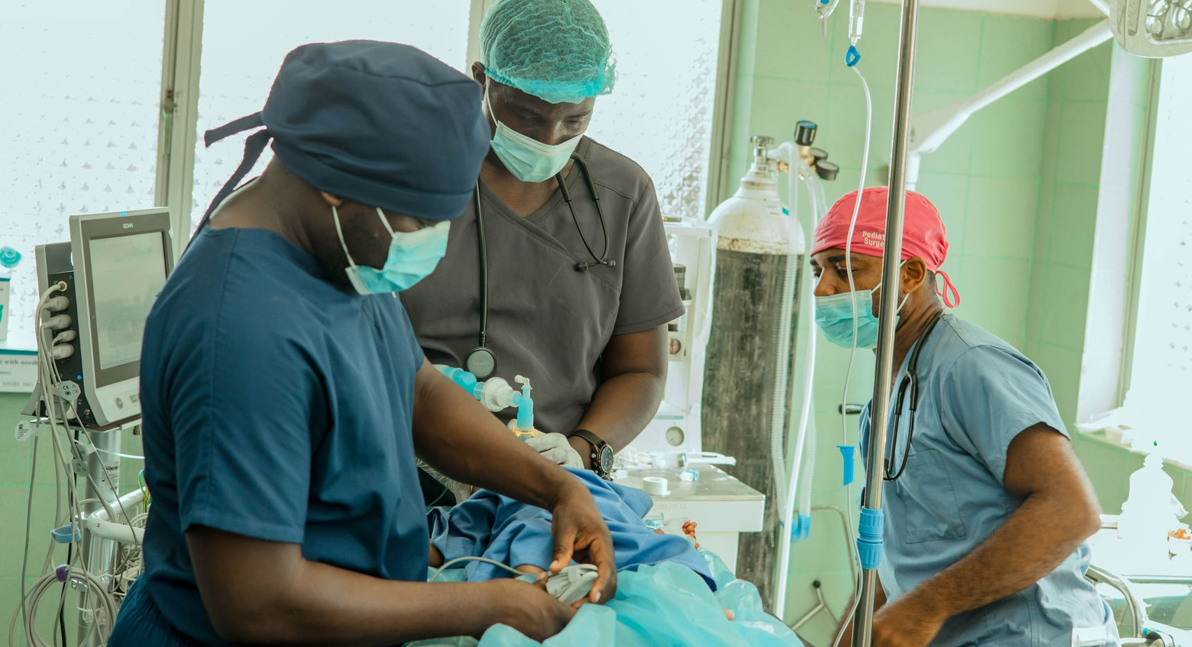 Three medical professionals in surgical attire tending to a patient in an operating room.