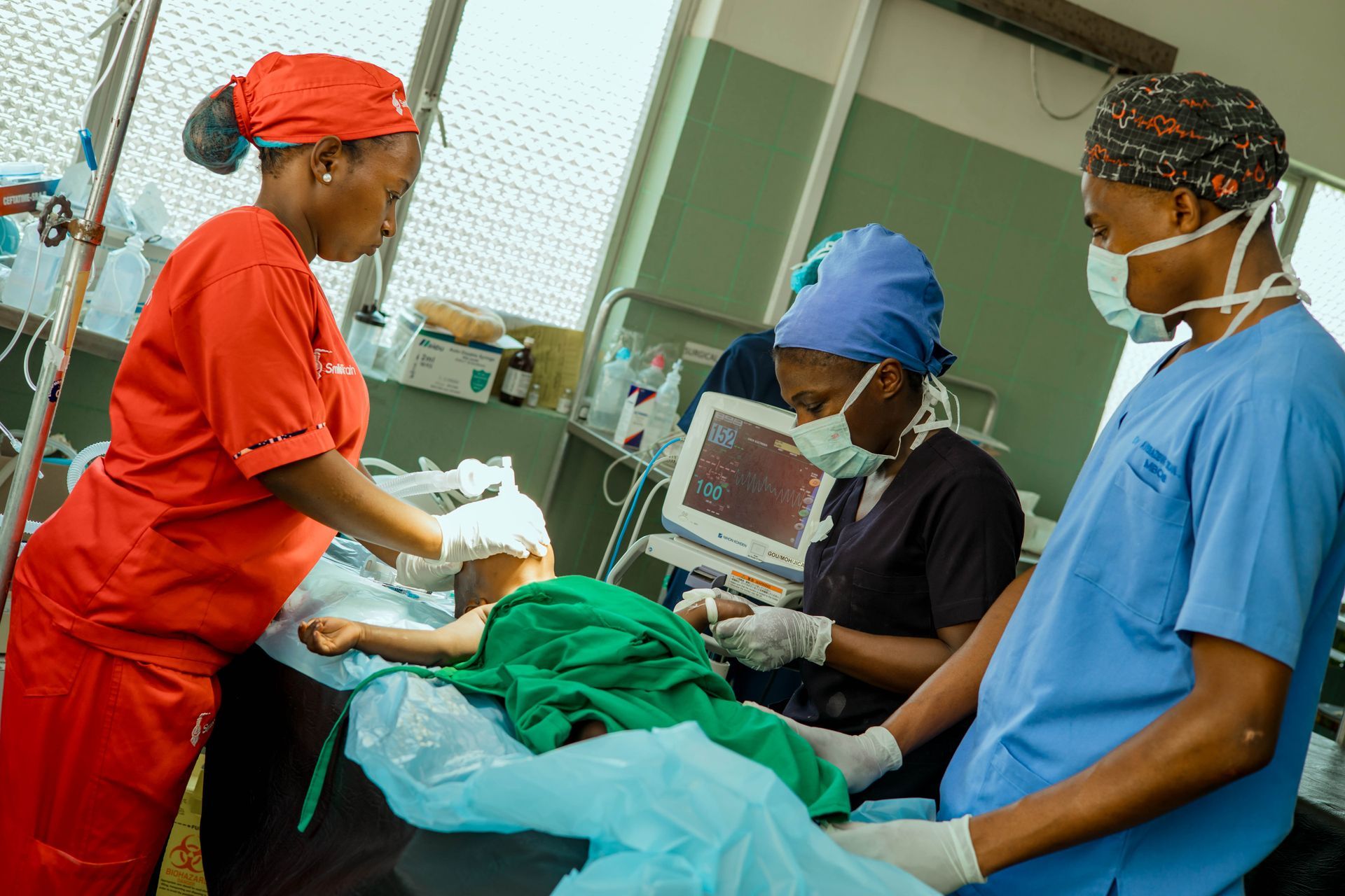 Medical team tending to a patient in an operating room. One nurse in red, others in scrubs.