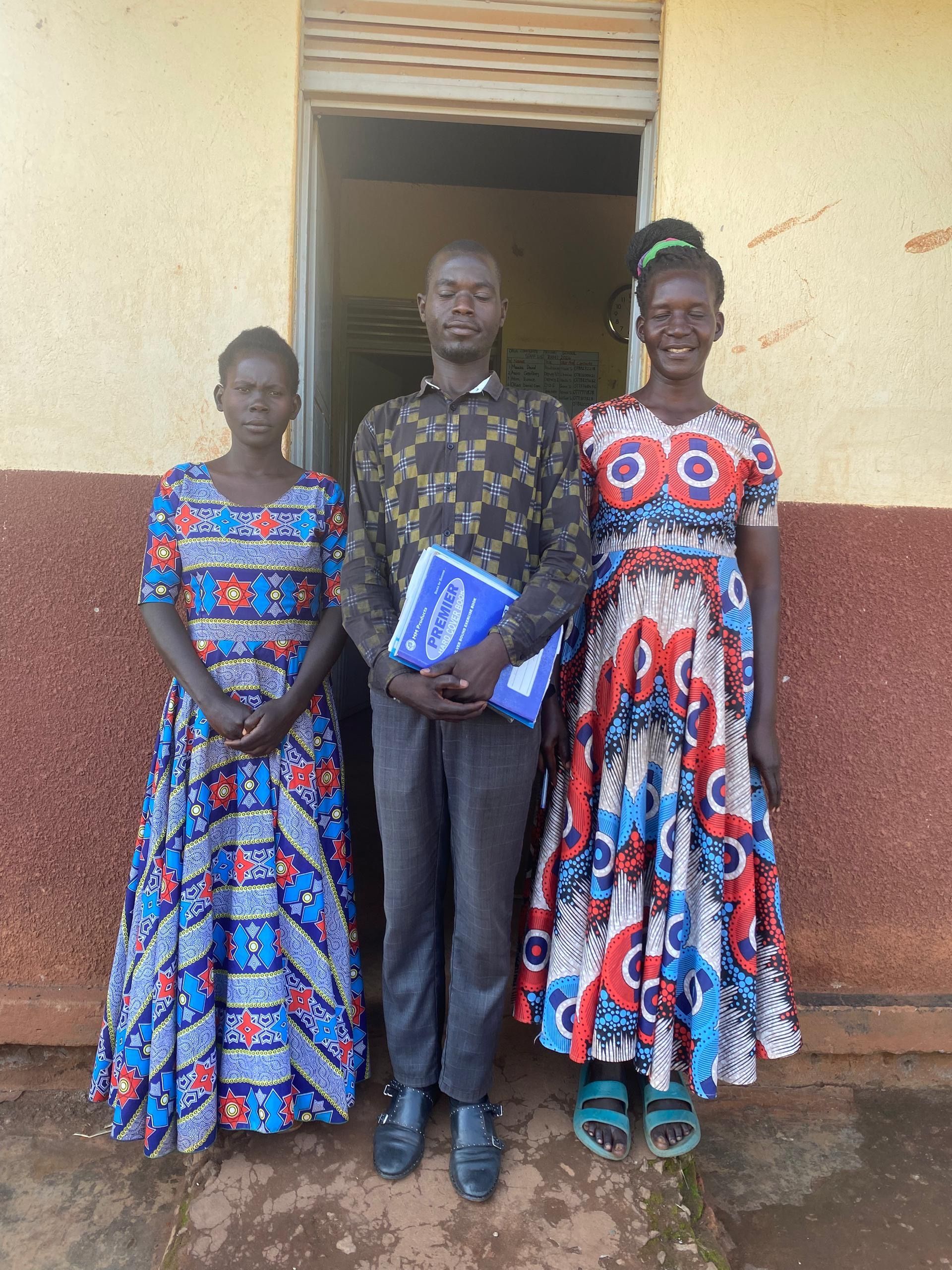 Korobar Village, Uganda — two women from the community in patterned Ugandan dresses on the school grounds, June 2026.