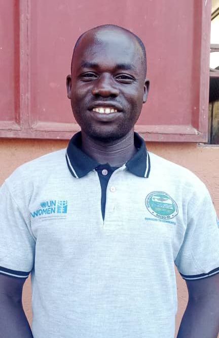 A man wearing a polo shirt is smiling and standing in front of a red wall.