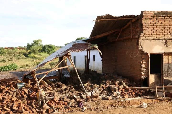 A brick building in a state of disrepair with a partially collapsed metal roof and debris scattered across the ground.