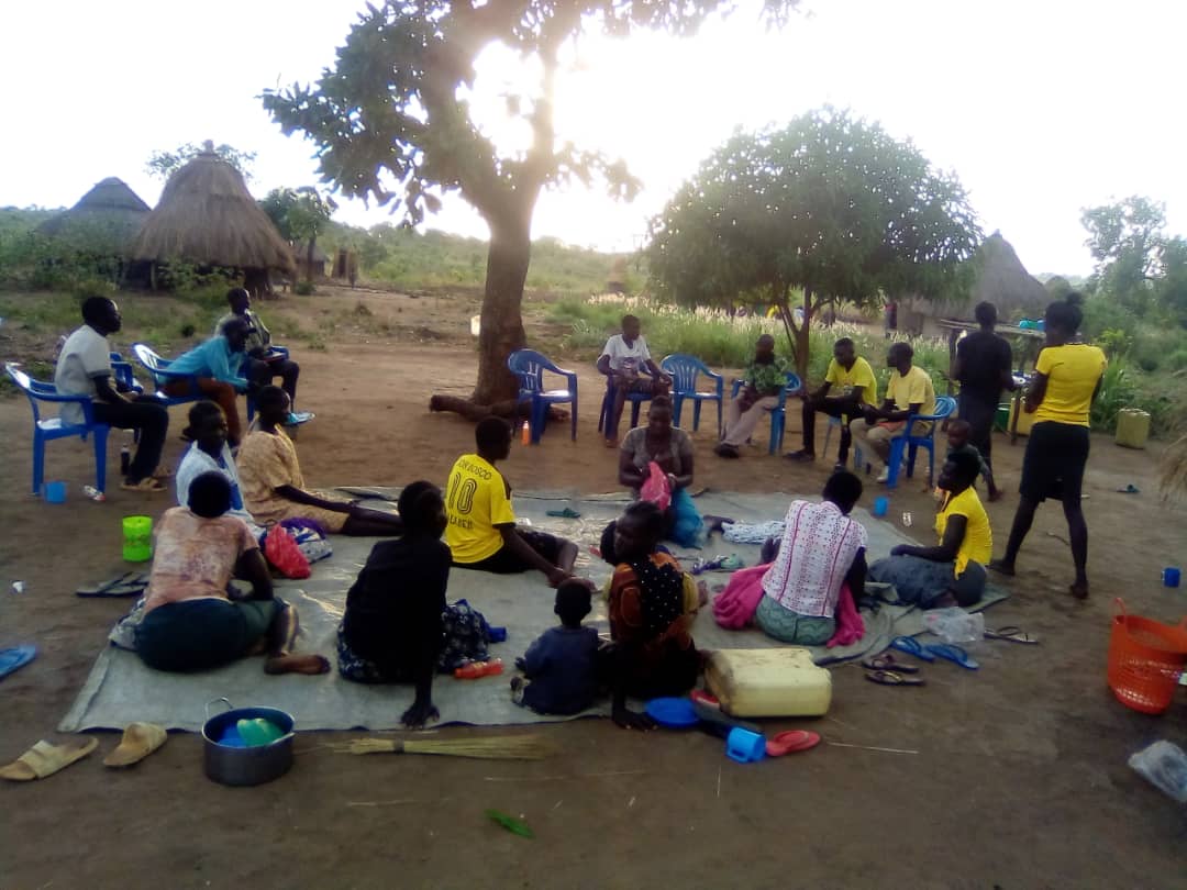 A group of people are sitting on the ground under a tree.