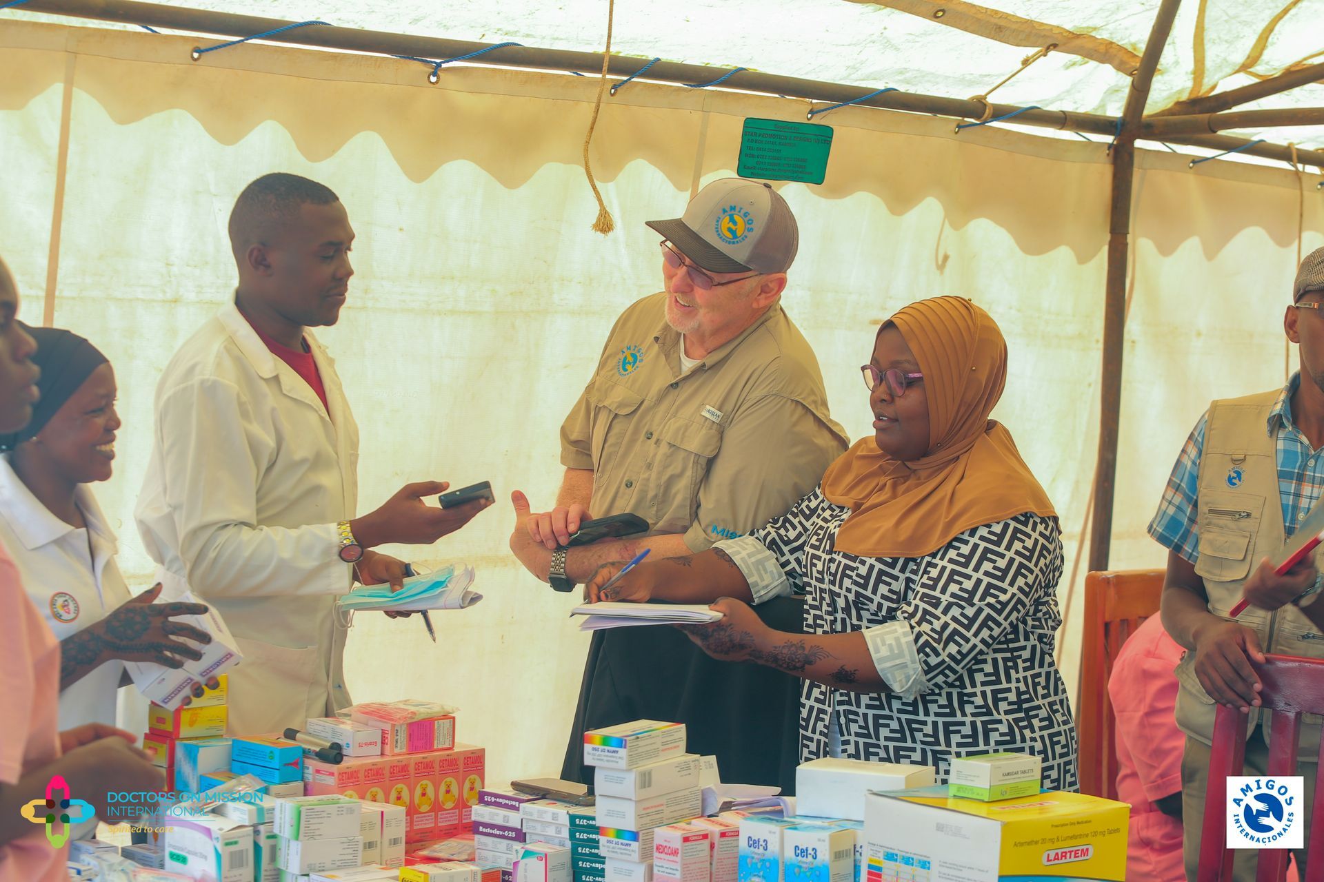 People at a medical clinic: doctors, patient, taking notes; medicines on table.
