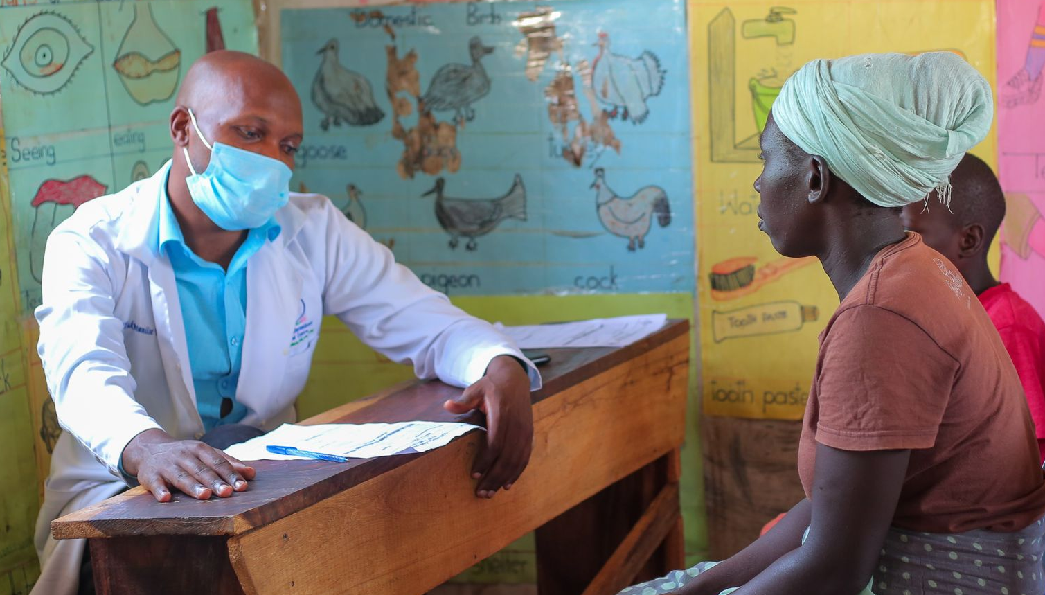 Doctor in a mask consulting with a woman, likely in a clinic or medical setting.