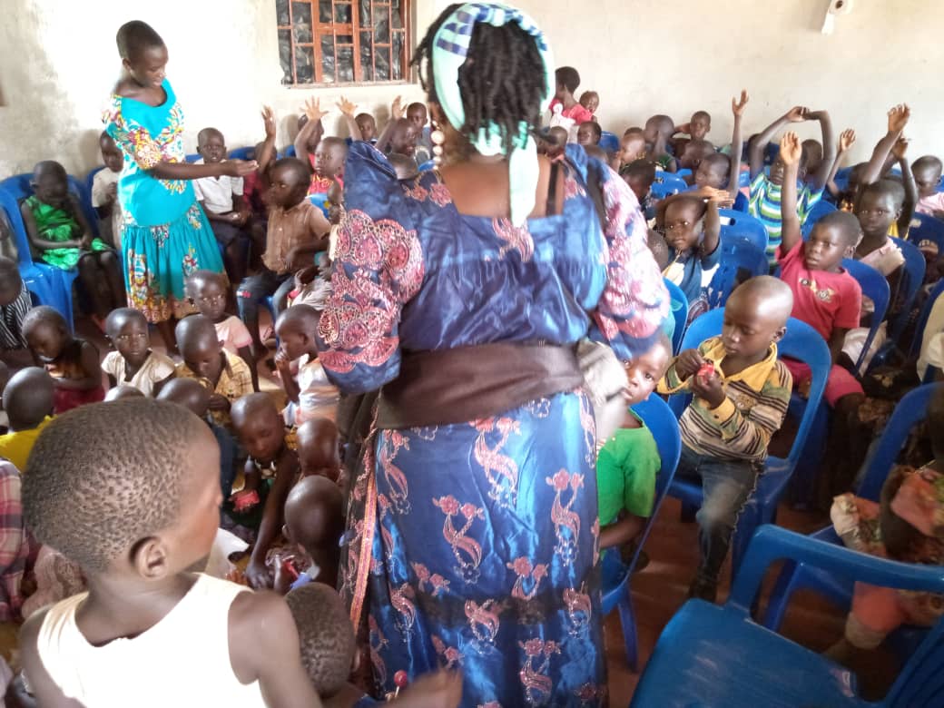 A woman in a blue dress is standing in front of a crowd of children