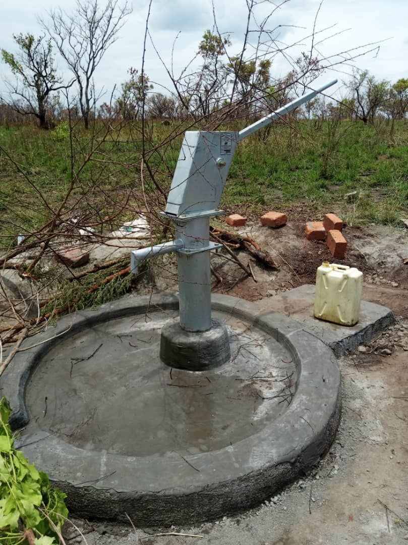 A water pump is sitting in the middle of a field.