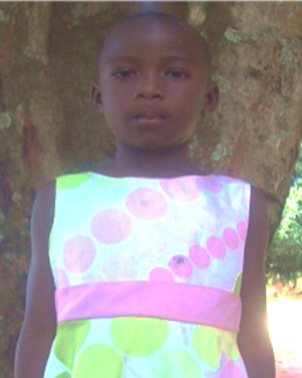 Girl wearing a sleeveless dress with pink and green circles posing in front of a tree.