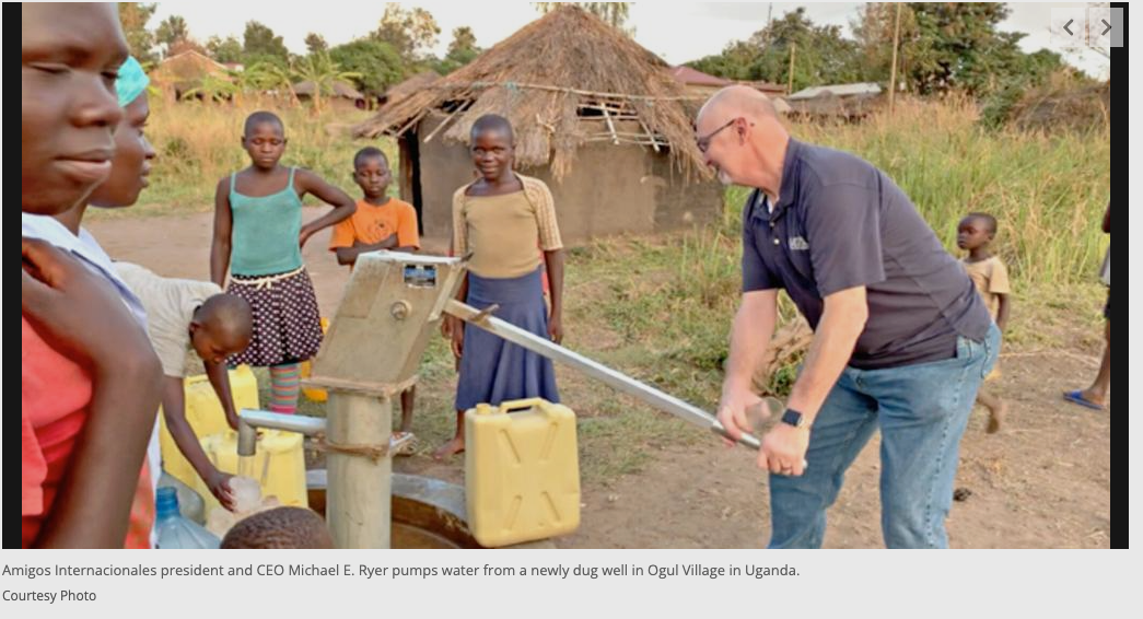 A man is pumping water from a well while children watch.