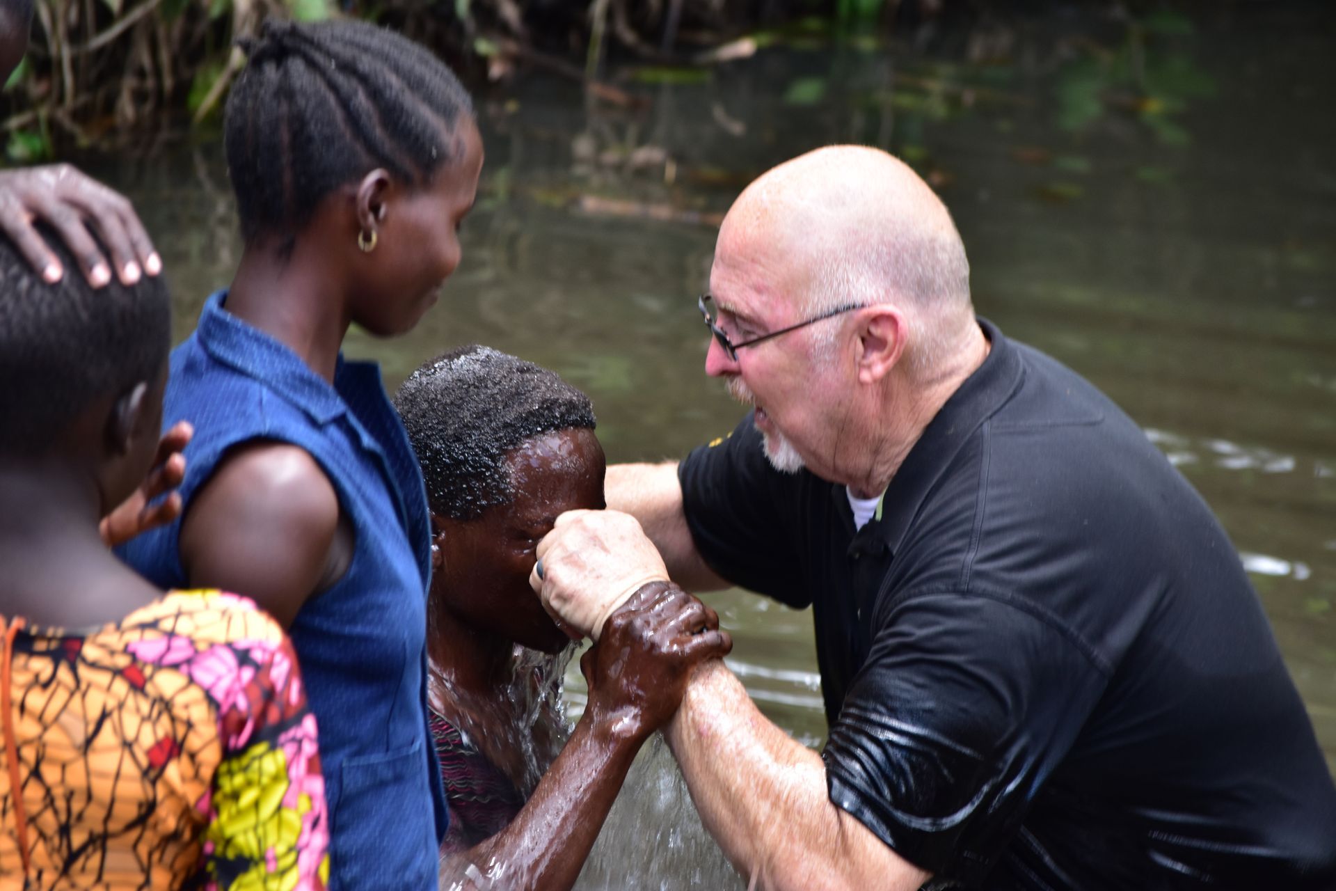 A man is baptising a young girl in a river.