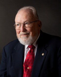 A man with glasses and a red tie is wearing a suit and tie.