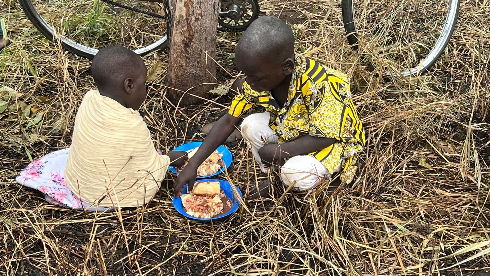 Two children are sitting on the ground eating food.