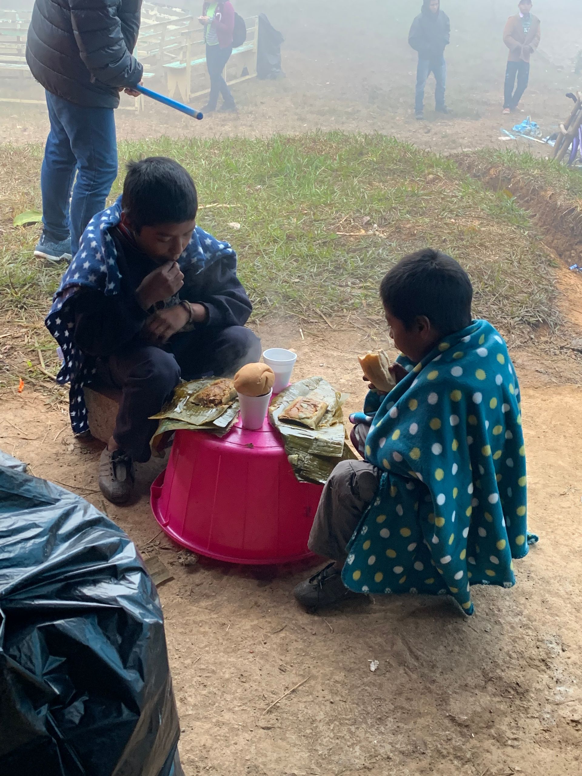 Two children are sitting on the ground eating food from a bowl.