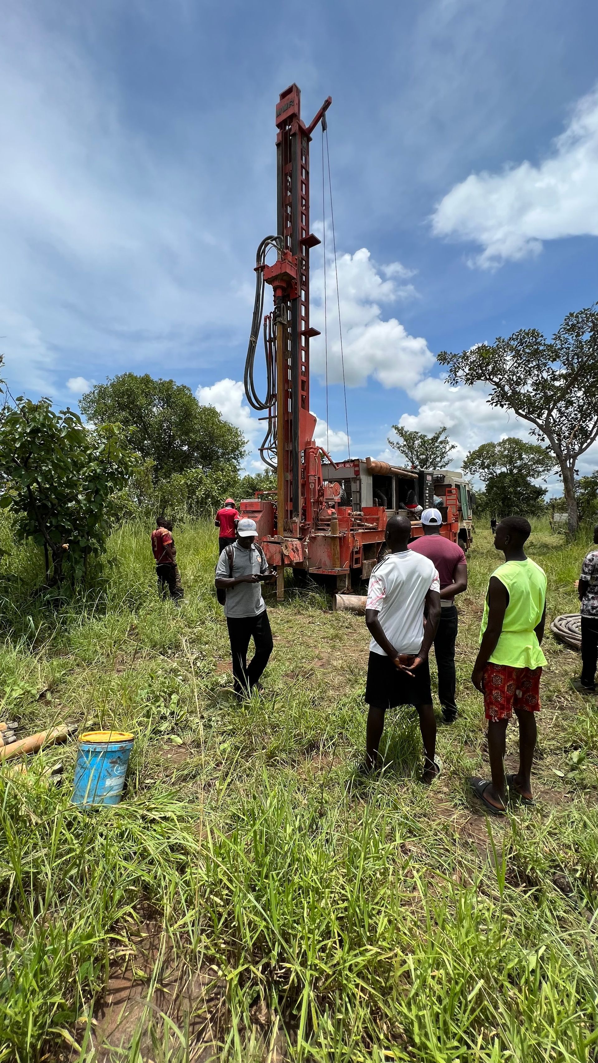 A group of people are standing around a drilling rig in a field.