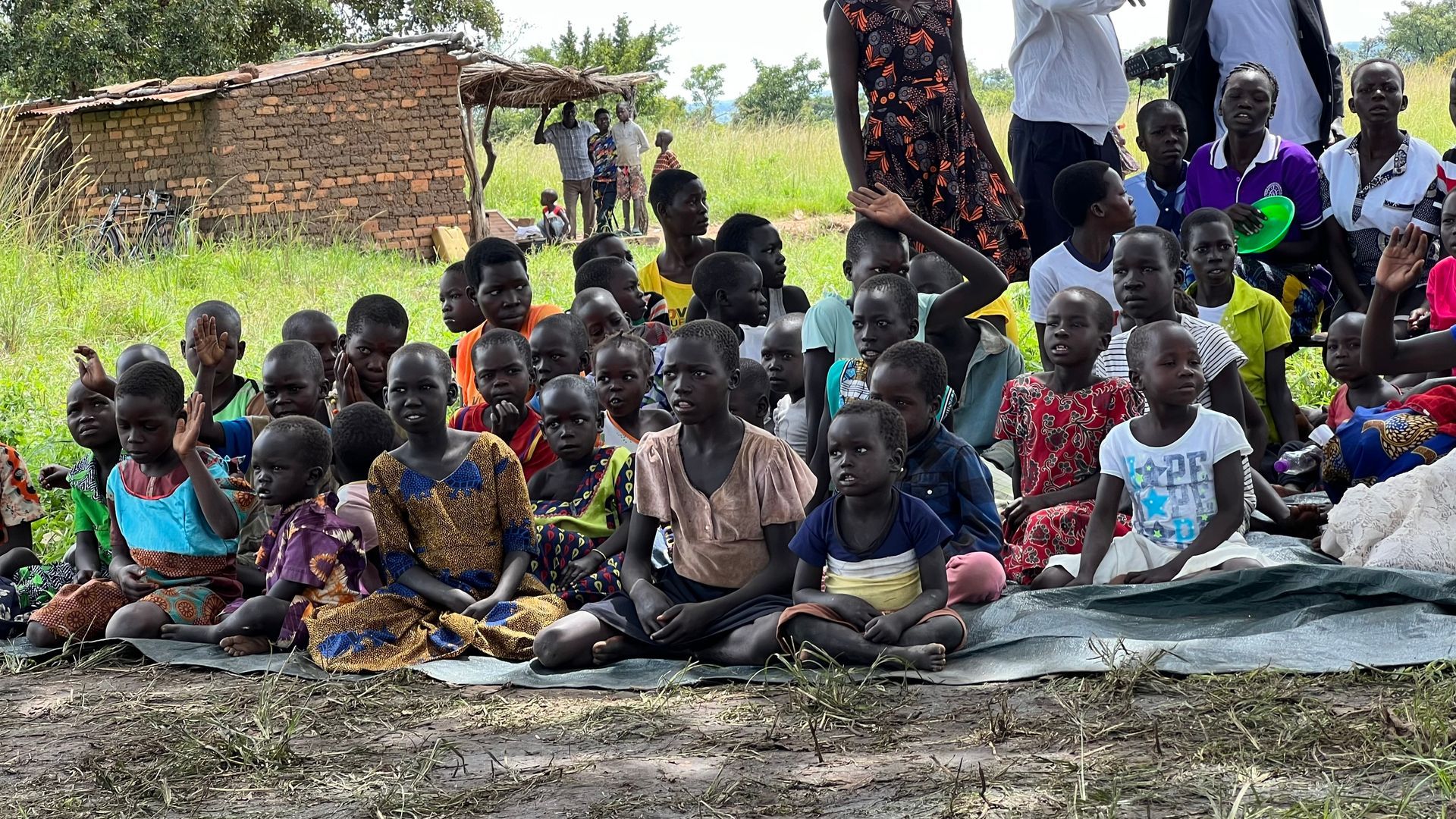 A group of children are sitting on the ground in a field.