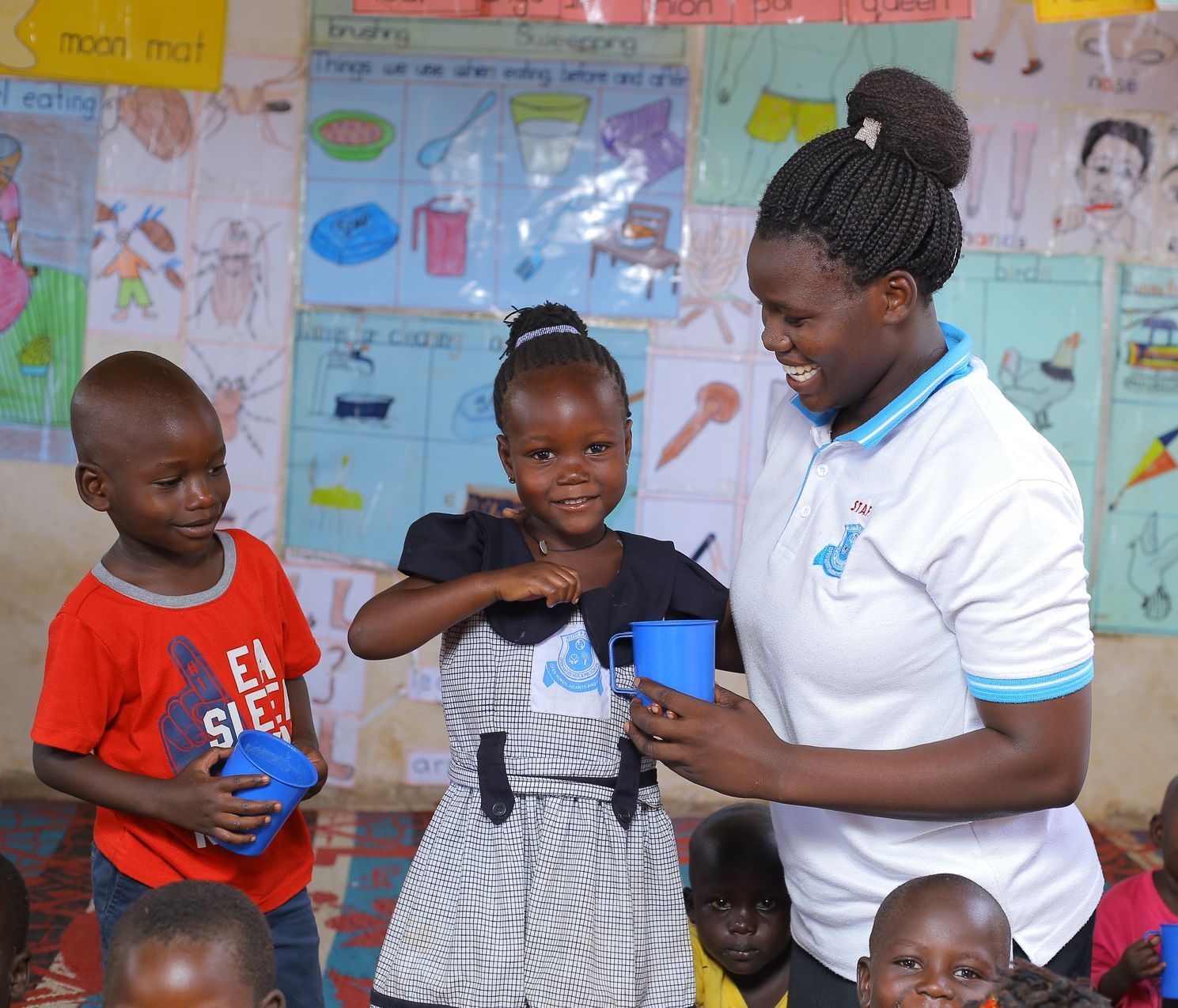 A woman is giving a cup to a little girl in a classroom.