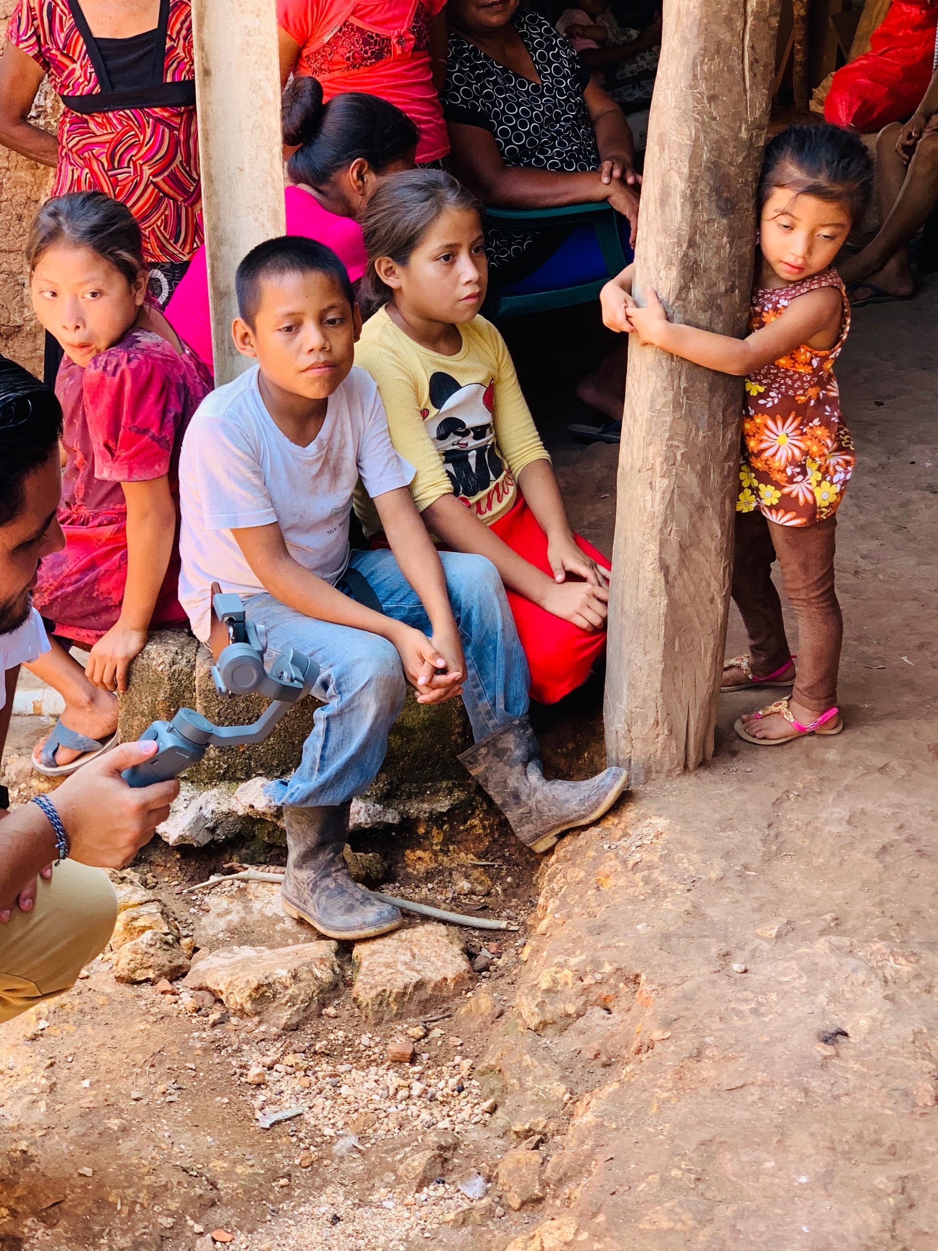 A group of children are sitting on a rock next to a pole.