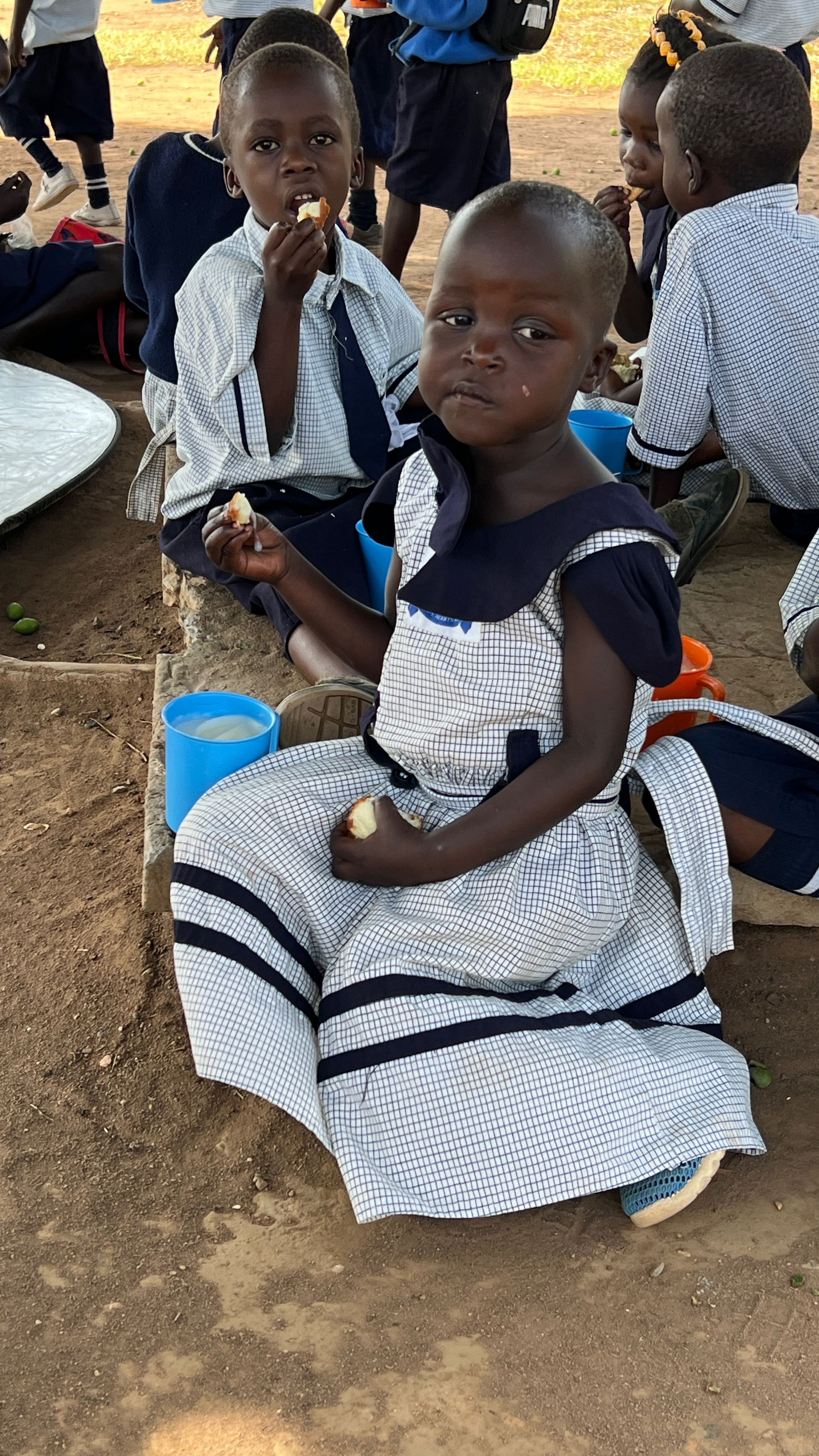 A group of children are sitting on the ground eating food.