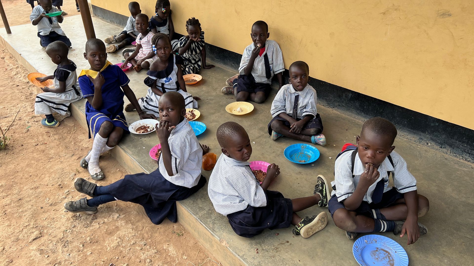 A group of children are sitting on the ground eating food.