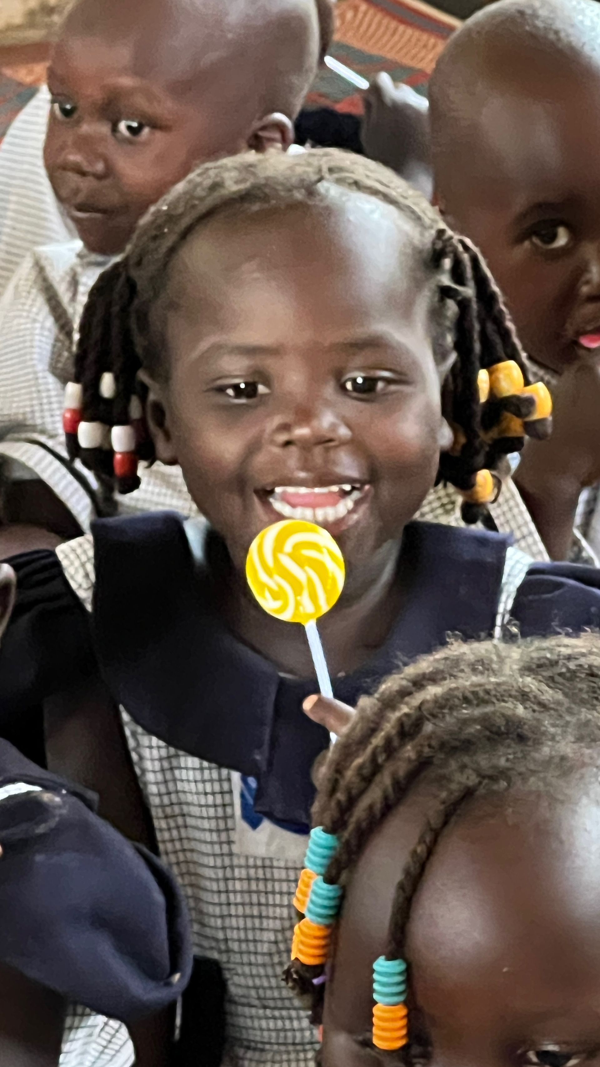 A little girl is holding a yellow lollipop in her mouth.