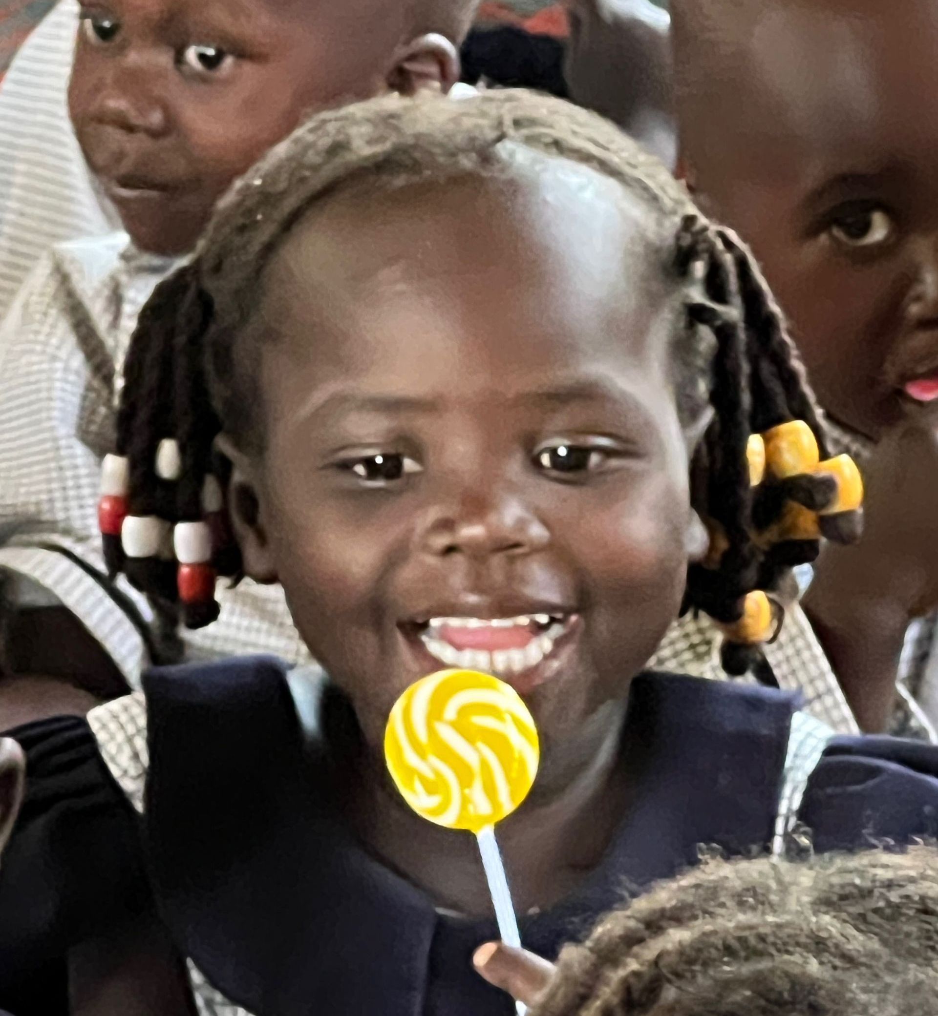 A little girl holding a yellow lollipop with the letter s on it