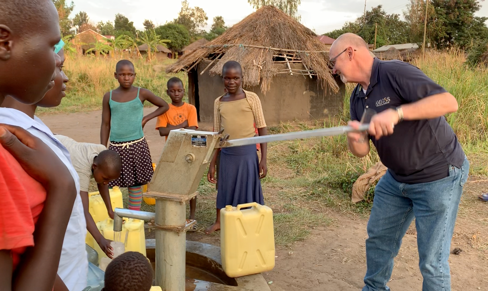 A man is pumping water from a well while children watch.