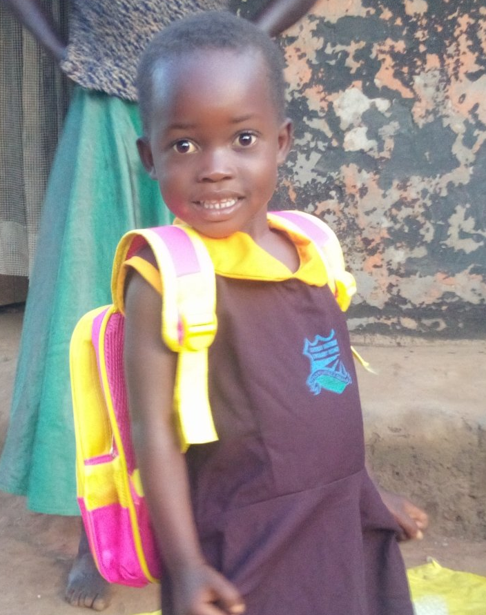 A child smiles while wearing a school uniform with a yellow collar and carrying a bright pink and yellow backpack.