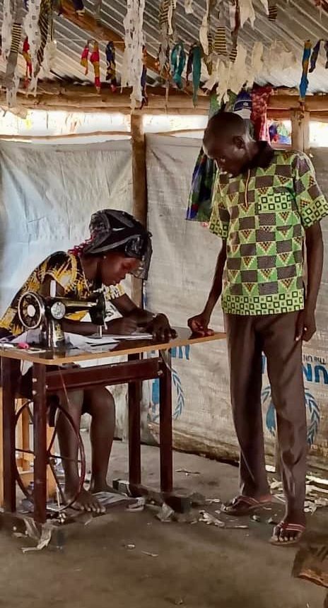 A man is standing next to a woman using a sewing machine.