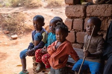 A group of children are sitting on a bench in front of a brick wall.