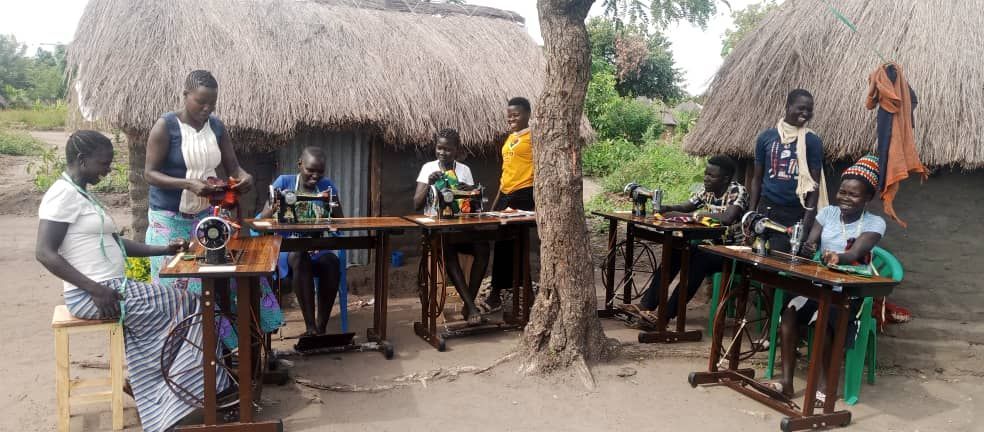 A group of people are sitting at tables using sewing machines.