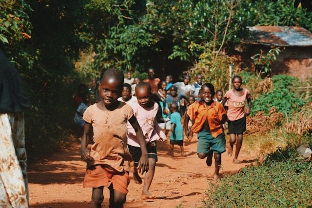A group of children are running down a dirt road.