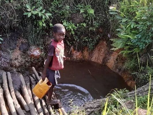 A young boy is standing next to a river holding a yellow bucket.