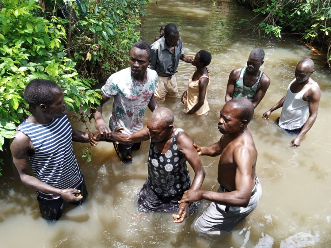 A group of men are standing in a river holding hands.