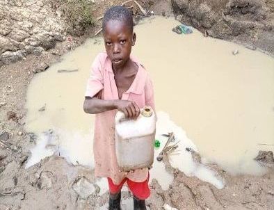 A young boy is standing in the mud holding a can of water.