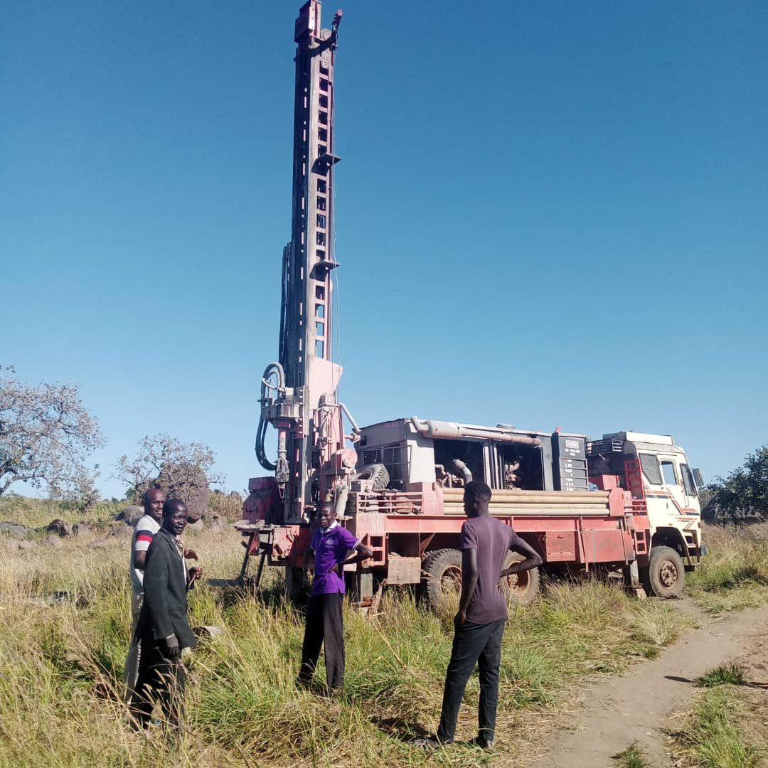 A group of people are standing in front of a truck in a field.