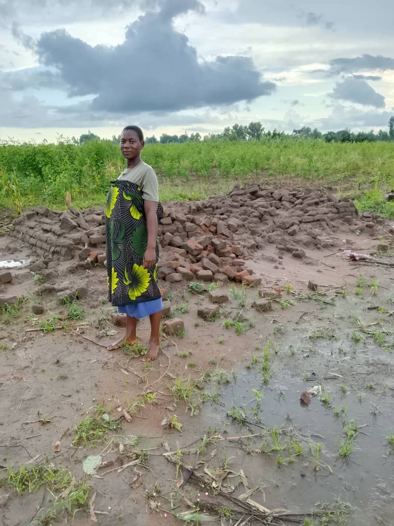 A person stands in a muddy, rural landscape near a pile of earth, under a cloudy sky.