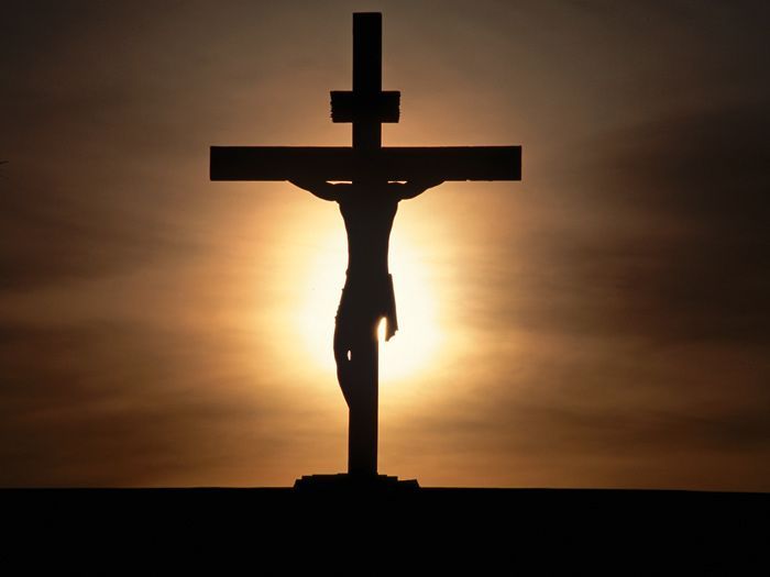 A silhouette of jesus on the cross with the sun behind him