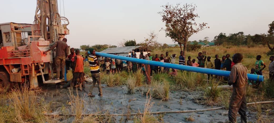 A group of people are standing around a large blue pipe in a field.