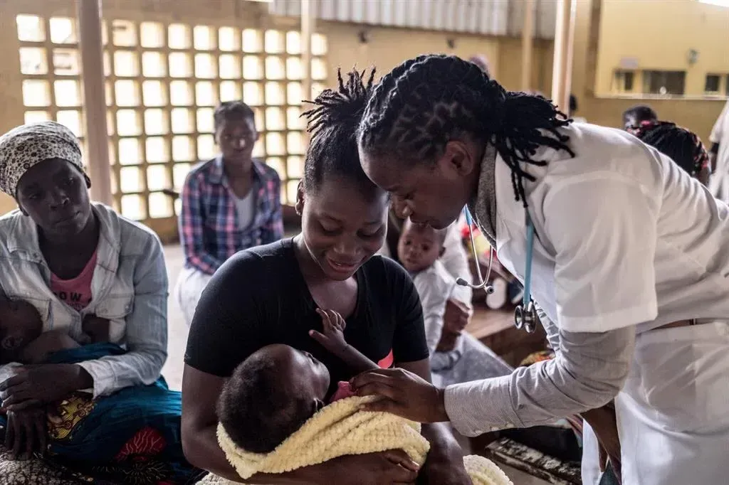A woman is holding a baby while a doctor examines it.