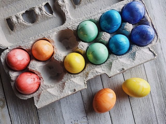 A carton of colorful easter eggs on a wooden table.