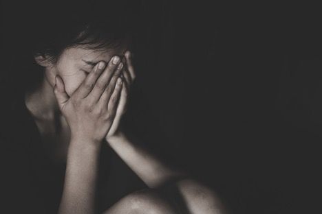 A woman is covering her face with her hands in a black and white photo.