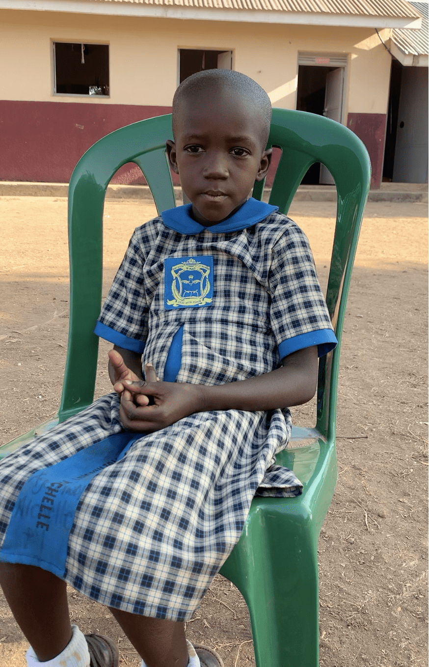 A young girl in a school uniform is sitting in a green chair.