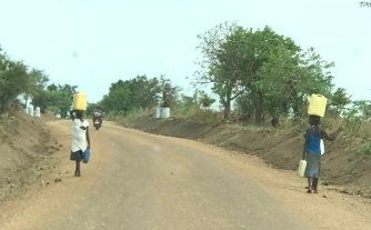 Two people are walking down a dirt road with buckets on their heads. Two people are walking down a dirt road with buckets on their heads.