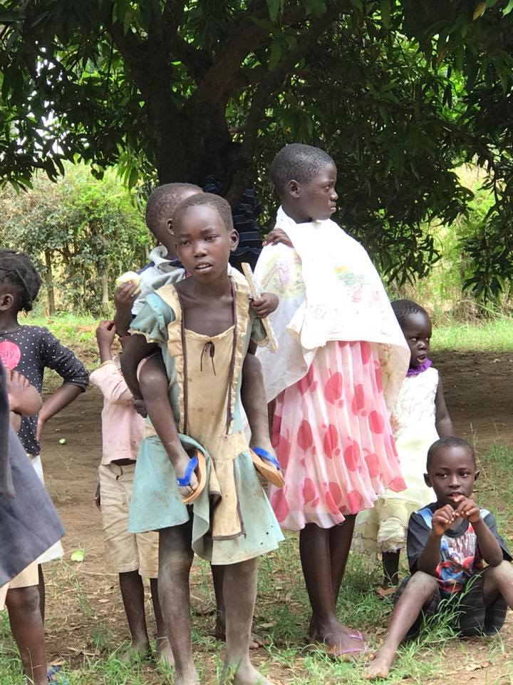 A group of children are standing in the grass under a tree.