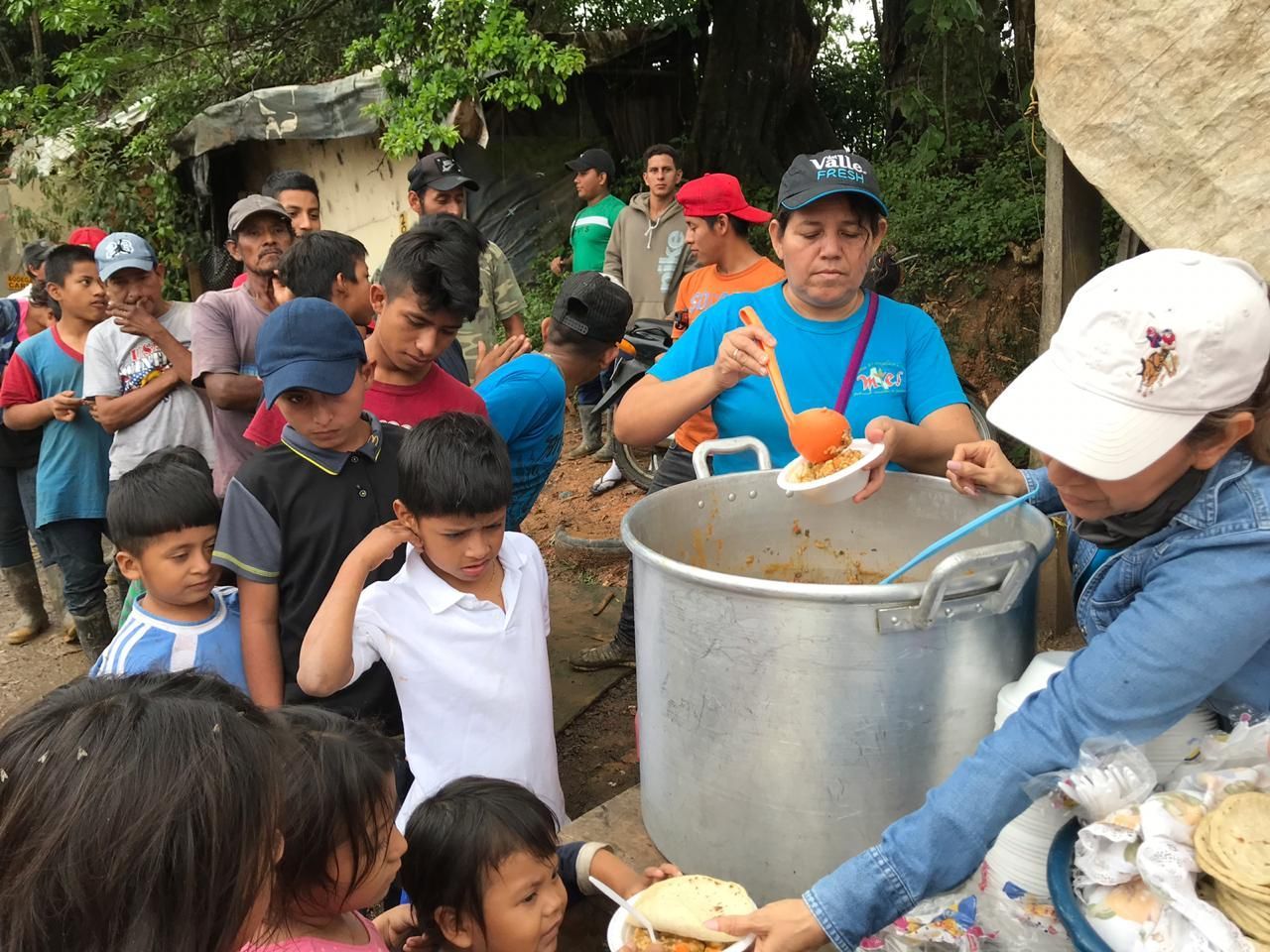 A group of people are standing around a large pot of food.
