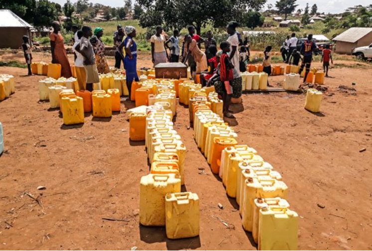 A group of people are standing around a row of yellow barrels filled with water. A group of people are standing around a row of yellow barrels filled with water.