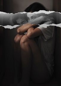 A woman is sitting on the floor with her arms around her knees.
